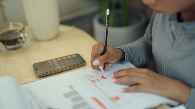Businesswoman Using Smartphone Calculator While Reviewing Financial Documents