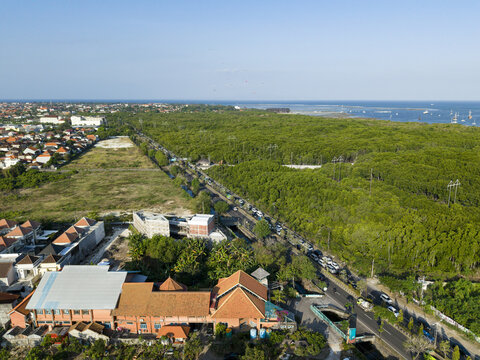 Aerial view of a traffic jam on Jl. Bypass Ngurah Rai with dense mangrove forest and residential buildings in Kecamatan Denpasar Selatan, Bali, Indonesia.