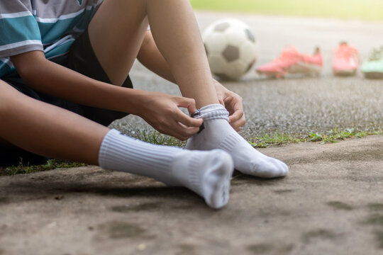 Close-up of a young soccer player pulling up white socks before football training outdoors.