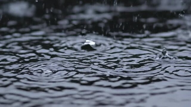 Heavy rain falling on water surface creating concentric ripples and splashes, moody dark atmosphere, close-up macro shot of stormy weather