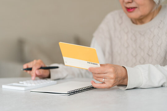 A senior woman uses a calculator to perform calculations (for retirement funds, living expenses, and pension) while looking at her savings passbook.