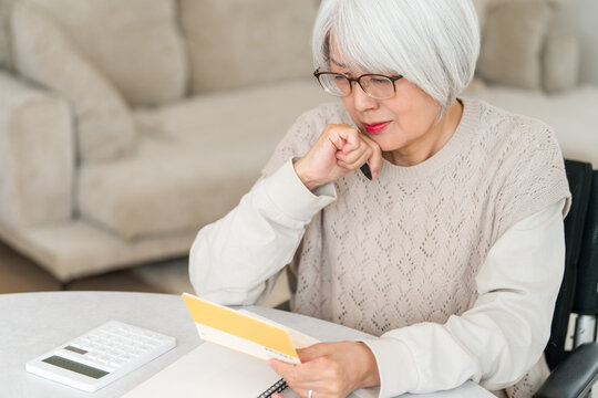 A senior woman uses a calculator to perform calculations (for retirement funds, living expenses, and pension) while looking at her savings passbook.