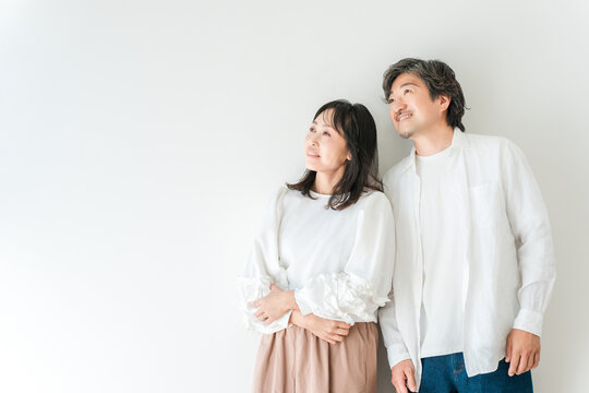 A smiling middle-aged couple, husband and wife, standing in front of a white background.