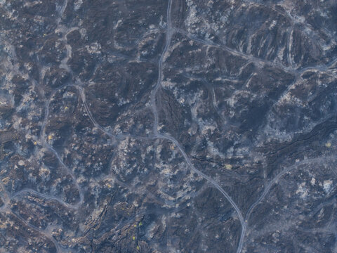 Aerial view of the volcanic landscape of Mount Batur, showing dark solidified lava flows, rugged terrain, and winding paths in Kintamani, Bali, Indonesia.