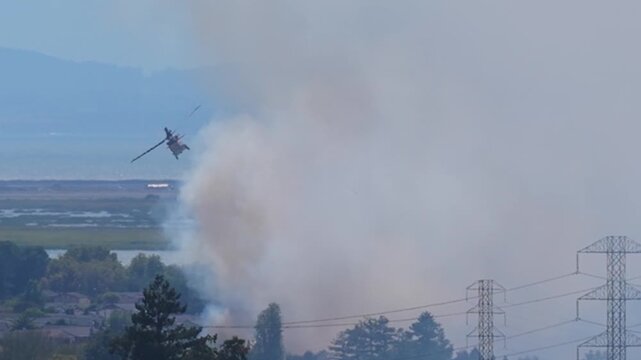 AMERICAN CANYON, CA - JULY 25, 2026: A firefighting helicopter works the Dutch Flat Fire as smoke thins to reveal homes, power lines and San Pablo Bay beyond, Napa County, California.