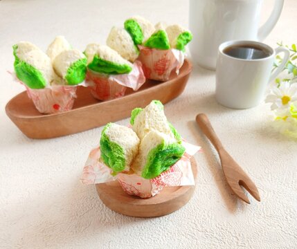 Traditional Indonesian steamed sponge cake, known as bolu kukus, with a distinctive flower-like shape and vibrant green and white colors, served in paper cups with a cup of black coffee. Soft, fluffy 
