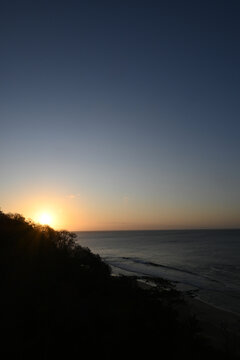 Aerial view of the sunset over the coastline of Fernando de Noronha with lush vegetation and calm ocean waves in Fernando de Noronha, Pernambuco, Brazil.