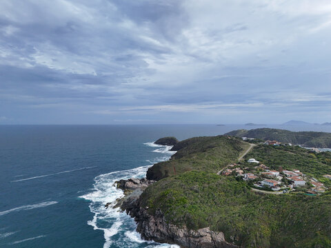 Aerial view of Praia da Foca with rocky cliffs, lush green vegetation, and coastal houses overlooking the Atlantic Ocean in Armacao dos Buzios, Rio de Janeiro, Brazil.