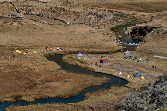 colorful tents rests peacefully on golden grassland at Jahuacocha campsite, dwarfed by the towering, glaciated face of Jirishanca deep in Peru's Cordillera Huayhuash