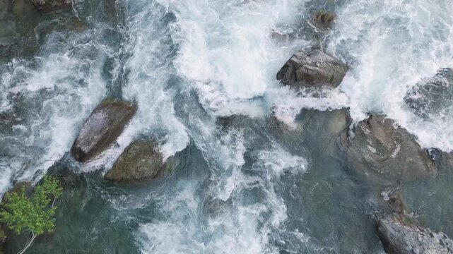 Aerial top down shot of wild river rapids splashing over rocks. Crystal clear blue running water cascading through a rocky streambed in a beautiful pristine nature landscape