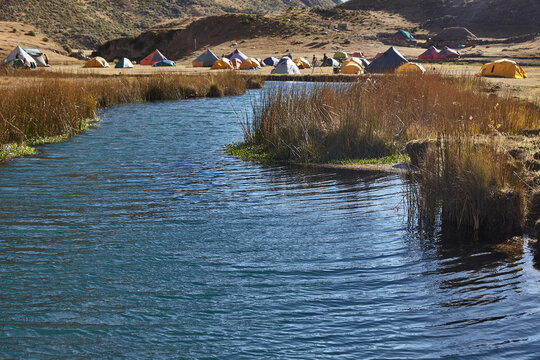 colorful tents rests peacefully on golden grassland at Jahuacocha campsite, dwarfed by the towering, glaciated face of Jirishanca deep in Peru's Cordillera Huayhuash