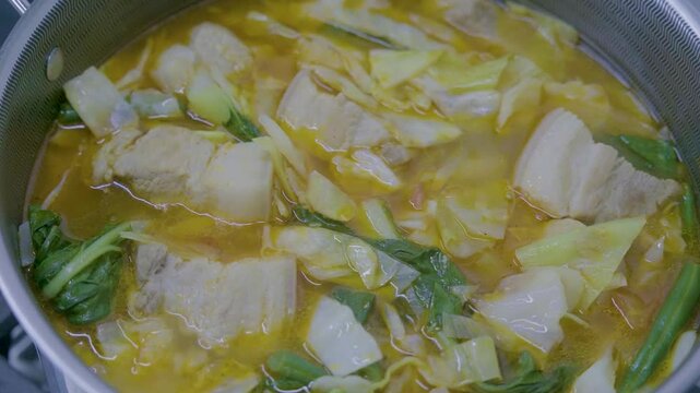 Cooking Filipino Pochero with pork, vegetables, and broth in a pot on a stove