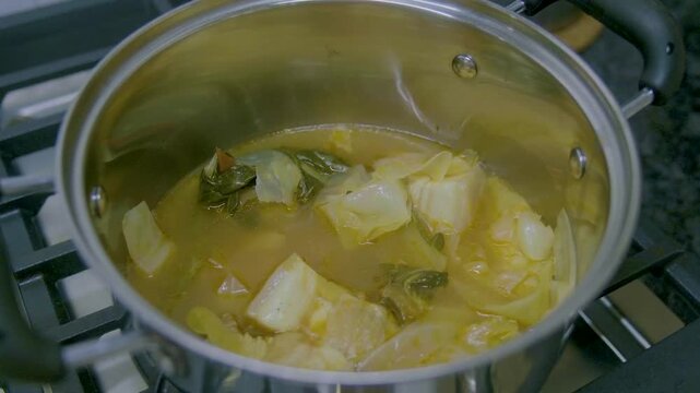Cooking Filipino Pochero with pork, vegetables, and broth in a pot on a stove