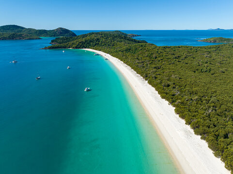 Aerial view of Whitehaven Beach with its pristine white sand and turquoise water surrounded by lush forest and boats in the Whitsunday Islands, Airlie Beach, Queensland, Australia.