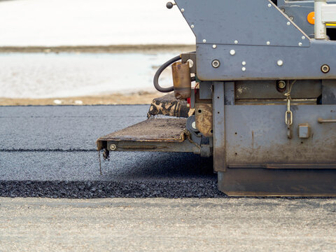 Heavy machinery asphalt paver spreading fresh hot bitumen layer during highway road resurfacing work.