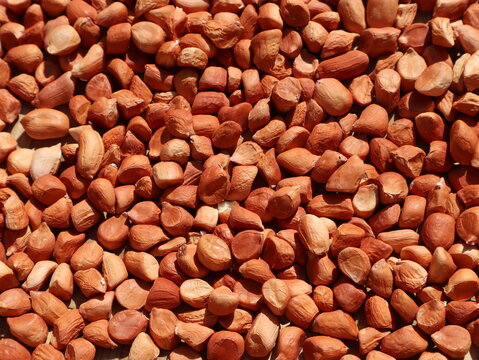 Raw shelled peanuts spread across a surface, showing whole and split peanut kernels with their natural reddish-brown skins and varied shapes.