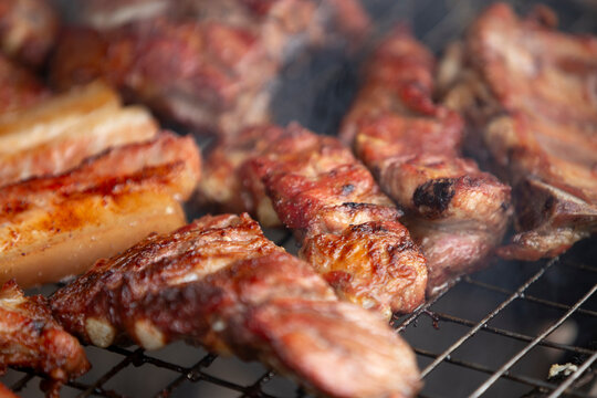 Close up of delicious pork ribs and belly grilling on a charcoal BBQ grate.A mouth-watering, close-up macro shot of seasoned pork ribs and thick pork belly slices grilling to perfection on a charcoal 