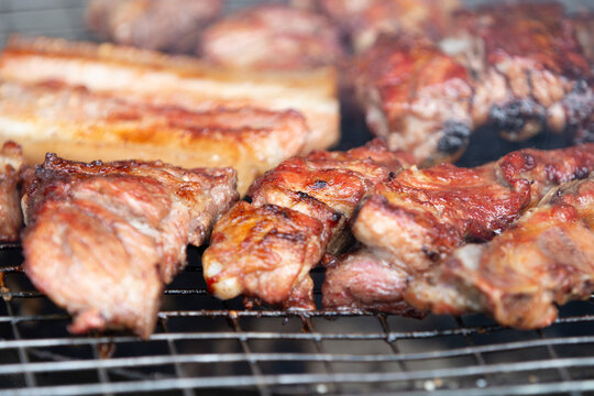 Close up of delicious pork ribs and belly grilling on a charcoal BBQ grate.A mouth-watering, close-up macro shot of seasoned pork ribs and thick pork belly slices grilling to perfection on a charcoal 