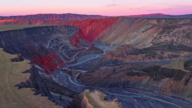 Aerial view of a deep gorge with a winding river and red cliffs at sunset in Anjihai Grand Canyon, Xinjiang, China