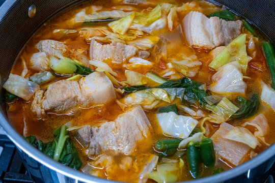 Cooking Filipino Pochero with pork, vegetables, and broth in a pot on a stove