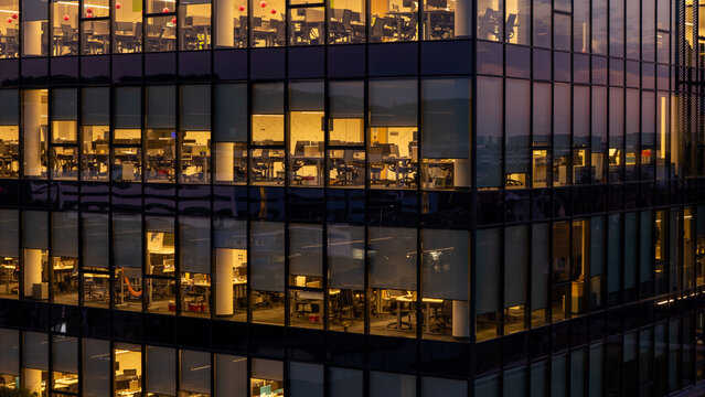 Aerial view of the illuminated glass facade of a modern office building with visible workspaces at dusk in Gdansk, Poland.