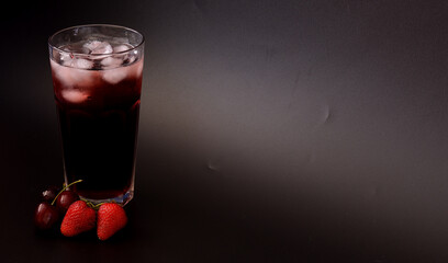 Tall glass of berry juice with ice on black background, ripe strawberries and cherries nearby. © Алексей Желтухин