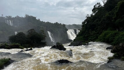 Majestic Iguazu Falls in Brazil with powerful cascades and lush green jungle under a cloudy sky © Felippe Lopes