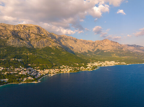 Aerial view of the coastal town of Brela nestled between the Adriatic Sea and the Biokovo mountains, featuring lush pine forests and rocky cliffs in Brela, Split-Dalmatia County, Croatia.