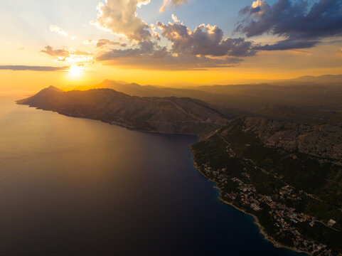 Aerial view of the Brela coastline at sunset with golden light illuminating the mountains and the Adriatic Sea in Brela, Split-Dalmatia County, Croatia.