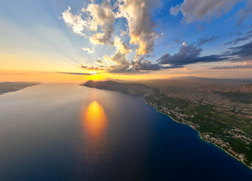 Aerial view of the Brela coastline at sunset with golden light reflecting on the Adriatic Sea, rocky cliffs, and coastal vegetation in Brela, Split-Dalmatia County, Croatia.