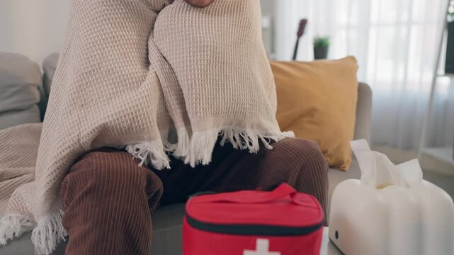 Latino sick man feeling cold while sitting on sofa in living room at home.