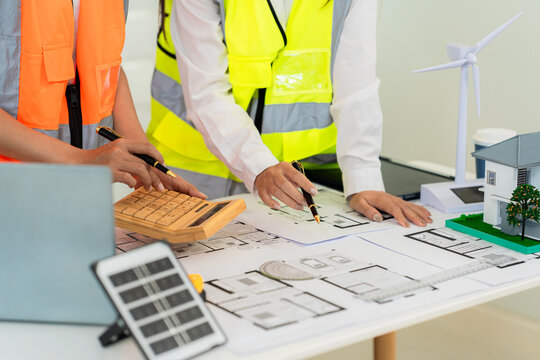 A team of architects and engineers is brainstorming an eco-friendly home design using a tablet, alongside a close-up view of a solar panel model.