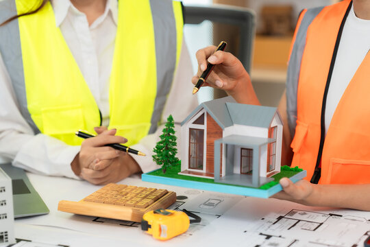 A team of architects and engineers is brainstorming an eco-friendly home design using a tablet, alongside a close-up view of a solar panel model.