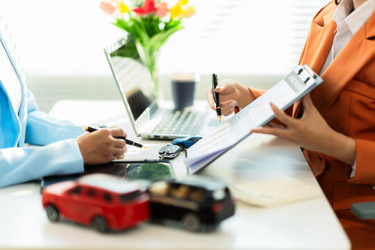A car dealer is explaining contract terms to a customer inside the office; a close-up shot of a salesperson showing vehicle purchase documents.