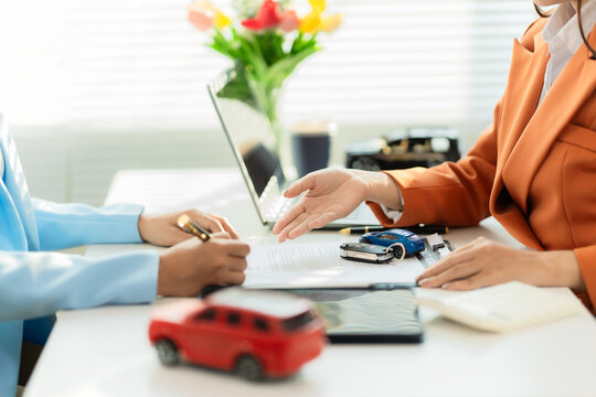 A car dealer is explaining contract terms to a customer inside the office; a close-up shot of a salesperson showing vehicle purchase documents.