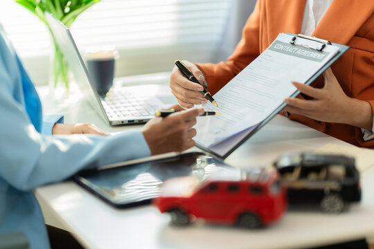 A car dealer is explaining contract terms to a customer inside the office; a close-up shot of a salesperson showing vehicle purchase documents.