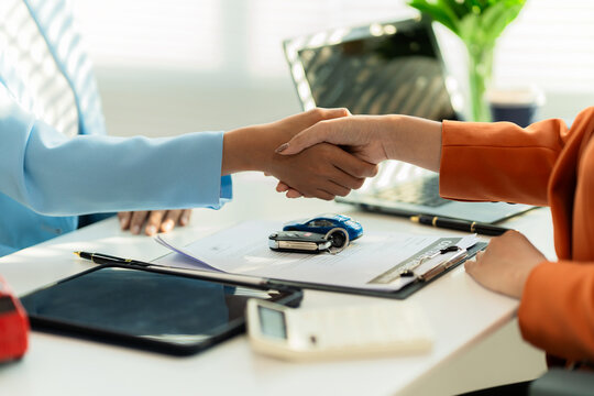 A close-up shot of a car dealer and a customer shaking hands over a business contract after signing the agreement.