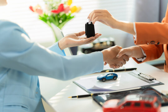 Close up of salesman giving key and shaking hands with customer after buying new car.
