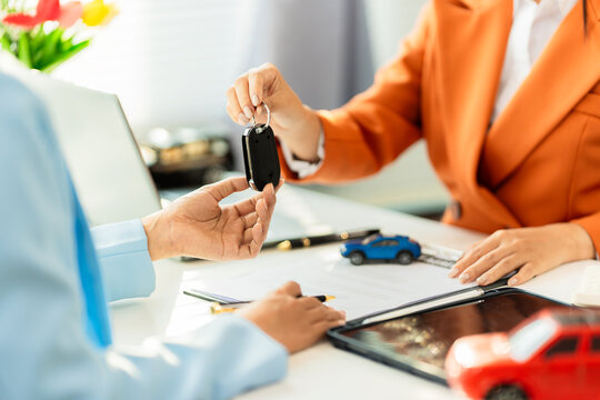 A car dealership hands over keys to a customer; a salesperson presents the remote key for a new car to the buyer in the showroom.