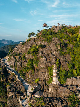 Aerial view of Mua cave with its iconic stone staircase winding up the karst mountain, featuring a pagoda at the summit and lush greenery in Nam Hoa Lu, Ninh Binh, Vietnam.