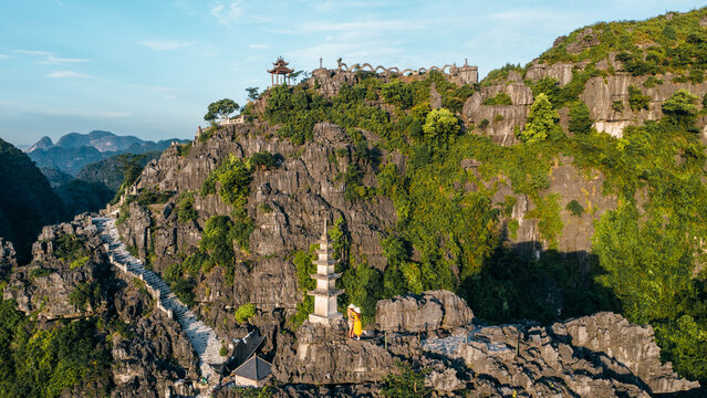 Aerial view of Mua Cave with its stone staircase winding up the limestone karst mountain, featuring a pagoda and dragon statue on the ridge, in Nam Hoa Lu, Ninh Binh, Vietnam.