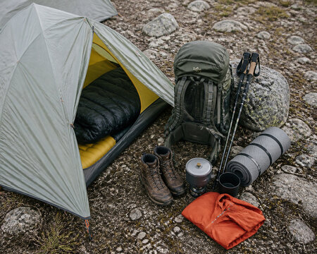 Tent, backpack, boots, gear set up on rocky ground. Tourism equipment for camping and hiking outdoor adventure. Concept of travel, nature, exploration and active lifestyle.