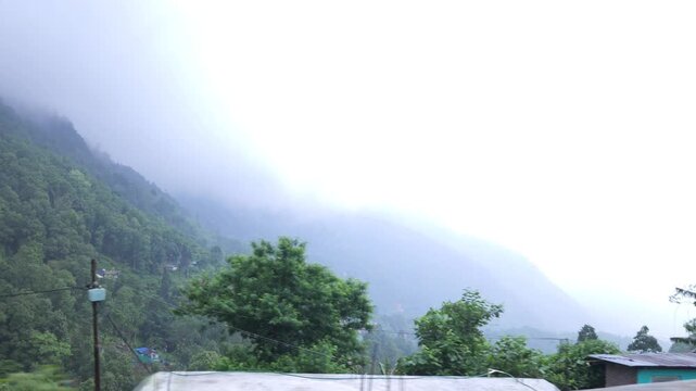 Dense fog and low clouds cover the lush green Darjeeling hills of West Bengal, India. Atmospheric Himalayan mountain landscape during monsoon weather, creating a peaceful and dramatic natural scene