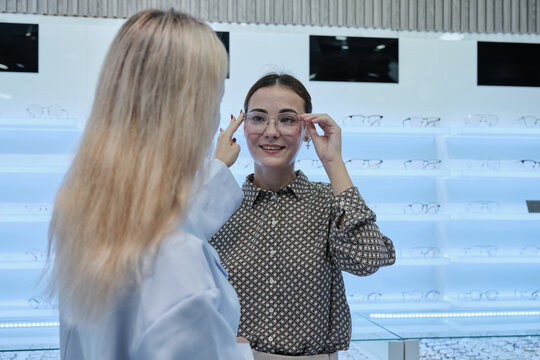 White female customer chooses eyeglasses with optometrist's help and guidance, improved eyesight for individual lifestyles, consults on decisions, and options choices at store display in optical shop.