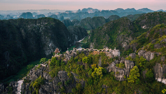 Aerial view of the Mua Cave dragon statue atop a limestone mountain ridge surrounded by lush greenery and winding river in Nam Hoa Lu, Ninh Binh, Vietnam.