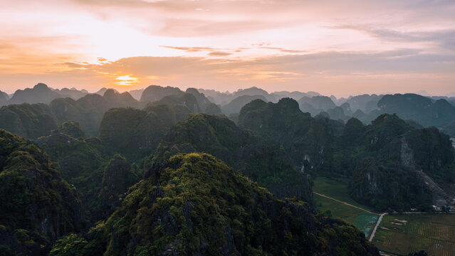 Aerial view of Mua cave surrounded by dramatic karst mountains and lush greenery under a golden sunset sky in Nam Hoa Lu, Ninh Binh, Vietnam.
