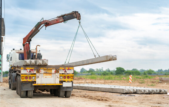 Heavy-duty boom truck lifting concrete posts and pillars from its flatbed for building site logistics and foundation work.