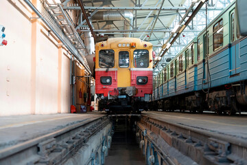 Obraz premium A vibrant yellow and red train sits on the tracks in a busy transit depot, with another blue train awaiting its turn in the background under bright lights