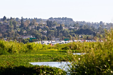 Fototapeta premium A green Santa Ana River corridor runs beside freeway traffic and hillside neighborhoods under clear summer skies in Yorba Linda.