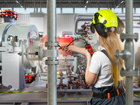 Industrial maintenance. Female technician uses diagnostic equipment to inspect pipelines, valves and machinery at a processing facility.